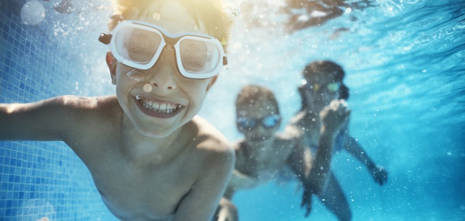 Symbolbild mit drei Kindern, die in einem Schwimmbecken Unterwasser tauchen